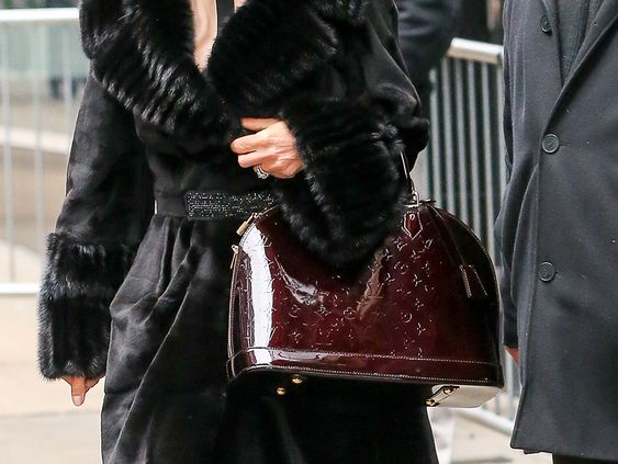 Mulher com casaco de pele preto carregando a Bolsa Verniz Wilshire Vinho.