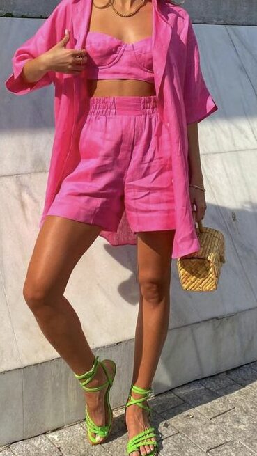 Modelo veste look de Carnaval: conjunto de top e shorts rosa, combinando com rasteirinha verde neon.
