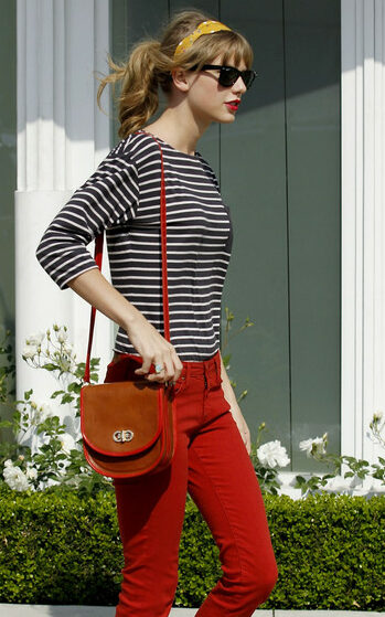 Look de Taylor Swift pelas ruas, combinando calça vermelha com blusa listrada, bolsa marrom e óculos escuros.