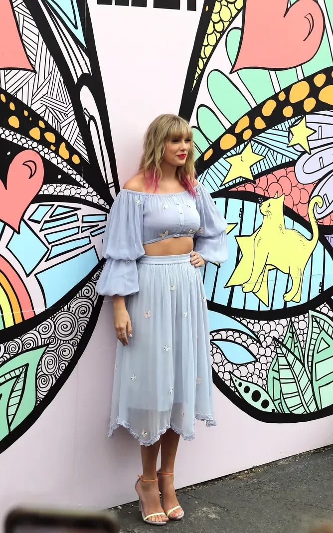 Taylor Swift veste um conjunto de cropped manga longa e bufante com saia midi, ambos na cor lilás.