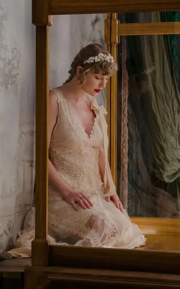 Taylor Swift na divulgação de Evermore, usando um vestido bege de renda e laços, combinando com uma coroa de flores.